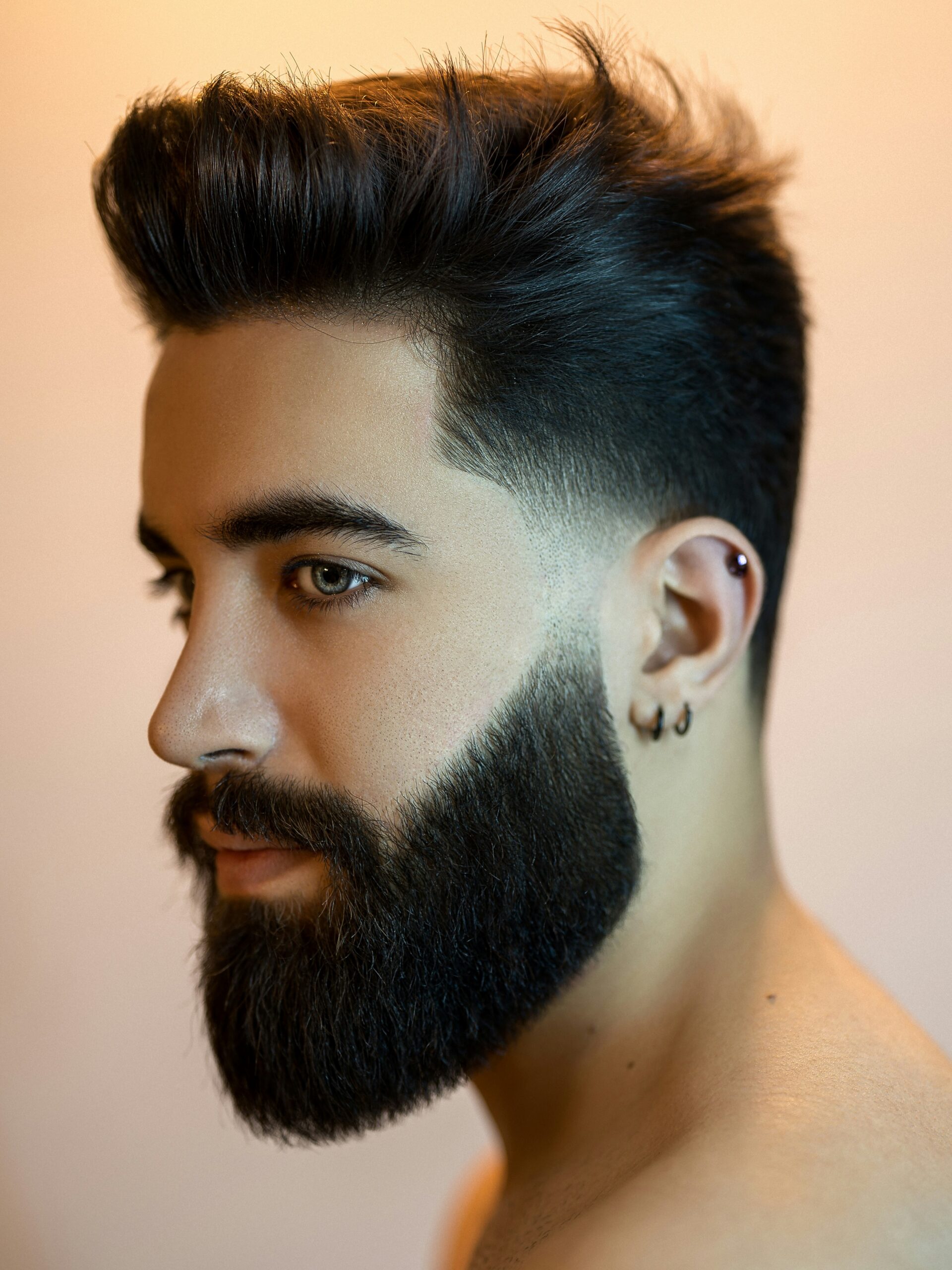Mann mit ovalem Gesicht und dunklem Haar, der einen Low Taper Fade mit Volumen und Bart trägt