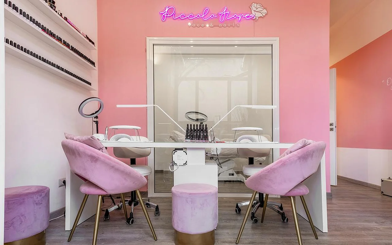Eine lebhafte Maniküre-Station mit knallpinken Wänden und einem pinkfarbenen Neonschild. Fliederfarbene Samtstühle mit goldenen Beinen stehen an einem minimalistischen weissen Tisch mit professionellen LED-Nagellampen.