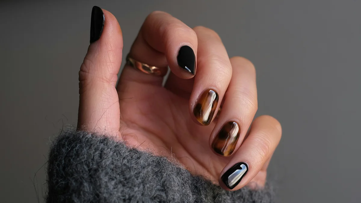 Nahaufnahme einer Hand mit kurzen Nägeln und glänzender Gel-Maniküre in Schwarz und Animal-Print