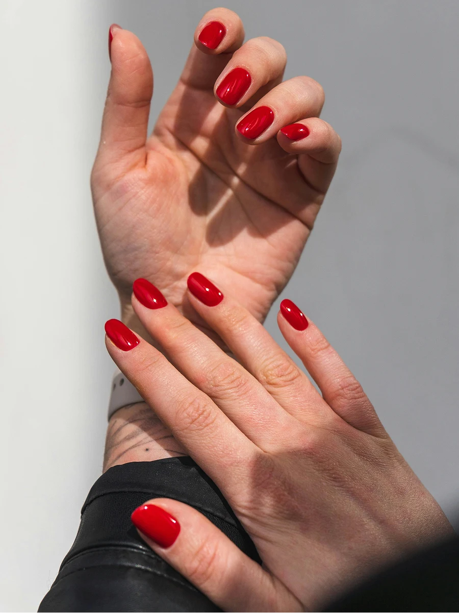 Nahaufnahme der Unterarme einer Frau in schwarzer Lederjacke mit glänzender roter Gel-Maniküre