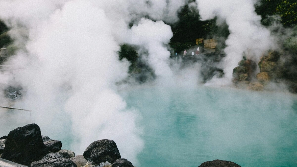 Weite Ansicht heisser Quellen in Japan, mit Dampfschwaden, die von einem von Felsen und Grün umgebenen Becken aufsteigen