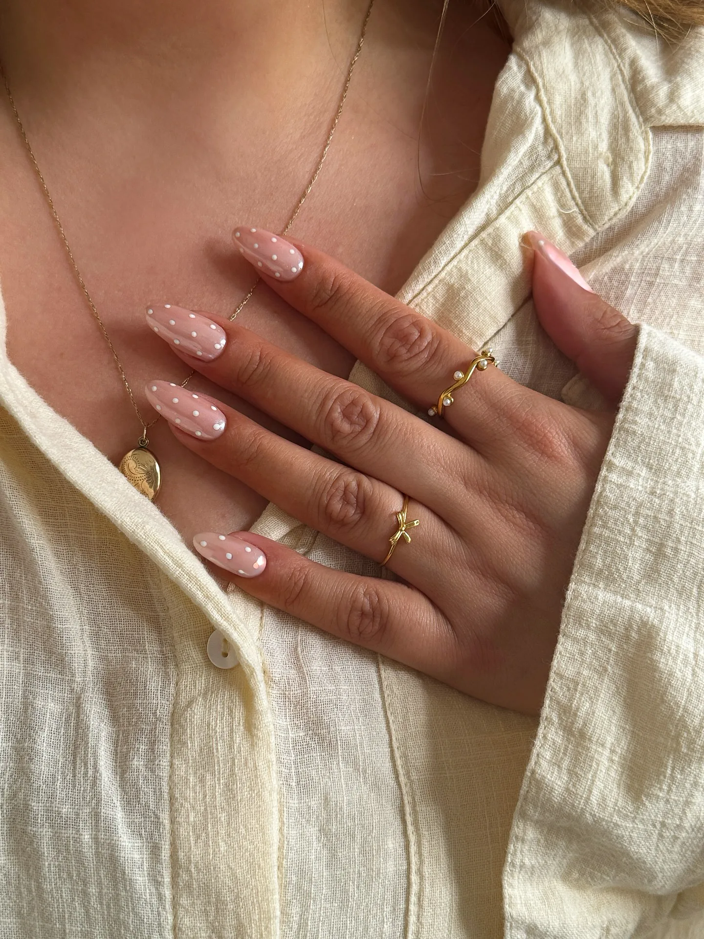 Mandelförmige Nägel auf transparent-rosa Basis, übersät mit gleichmässig verteilten weissen Mini-Punkten.