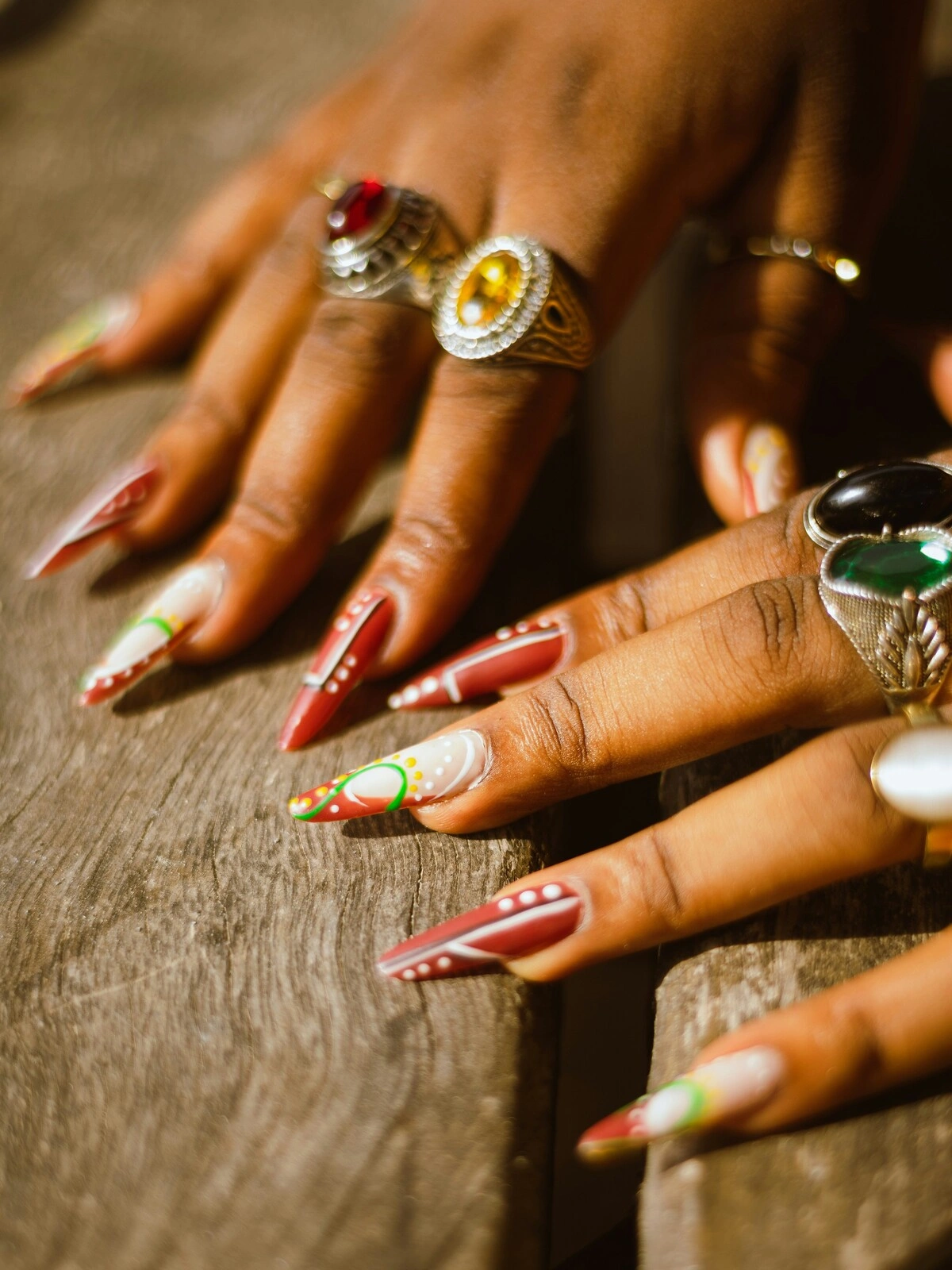Nahaufnahme der Hände einer Frau mit Acrylnägeln in Stiletto-Form in Rot und Weiss, verziert mit grünen und gelben Punkten und Schwüngen