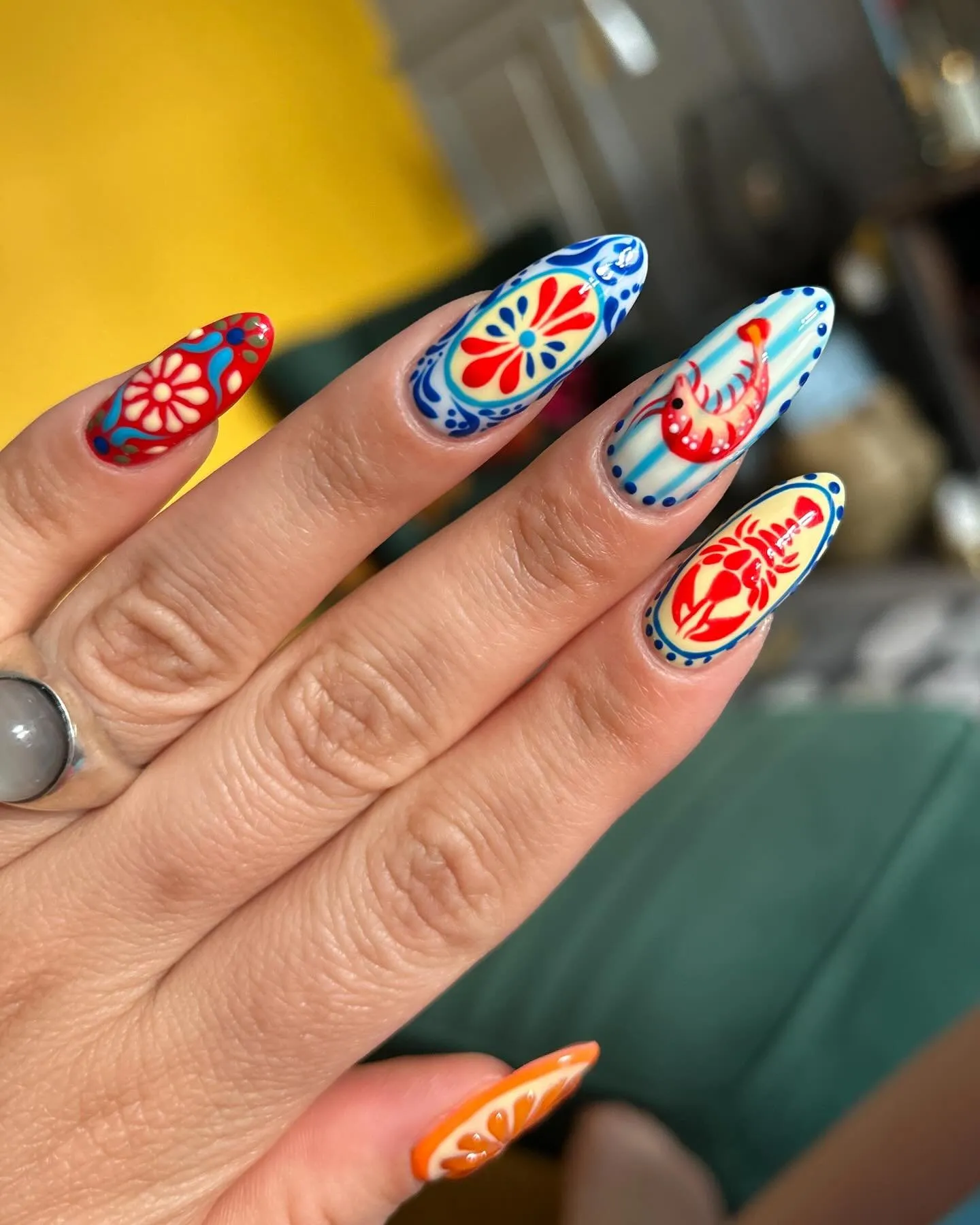 Destination-Nailart auf mandelförmigen Nägeln mit mediterran inspirierten Motiven in Rot, Blau und Orange