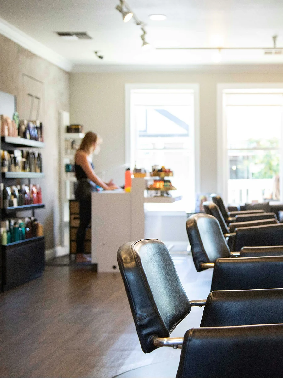 Innenaufnahme eines sauberen, hellen und gut belüfteten Friseursalons mit grossen Fenstern, schwarzen Stühlen und Produktregalen