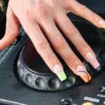 Eine Hand mit der Electric Mani auf dem Jog Wheel eines Pioneer-DJ-Players, neonfarbene French Tips mit Animal-Print und Swirls