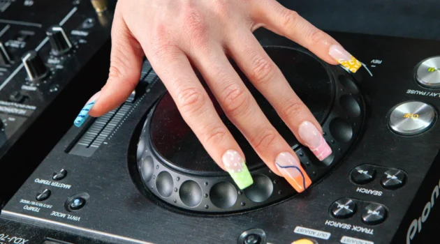 Eine Hand mit der Electric Mani auf dem Jog Wheel eines Pioneer-DJ-Players, neonfarbene French Tips mit Animal-Print und Swirls