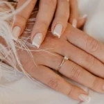 Klassische weisse French-Tip-Maniküre auf naturbelassenen, eckig gefeilten Nägeln auf weissem Stoff