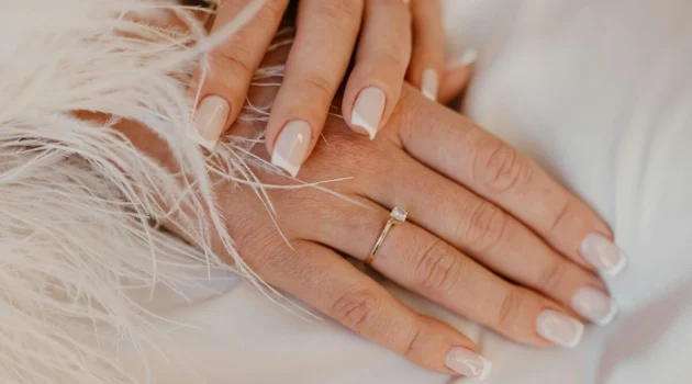 Klassische weisse French-Tip-Maniküre auf naturbelassenen, eckig gefeilten Nägeln auf weissem Stoff