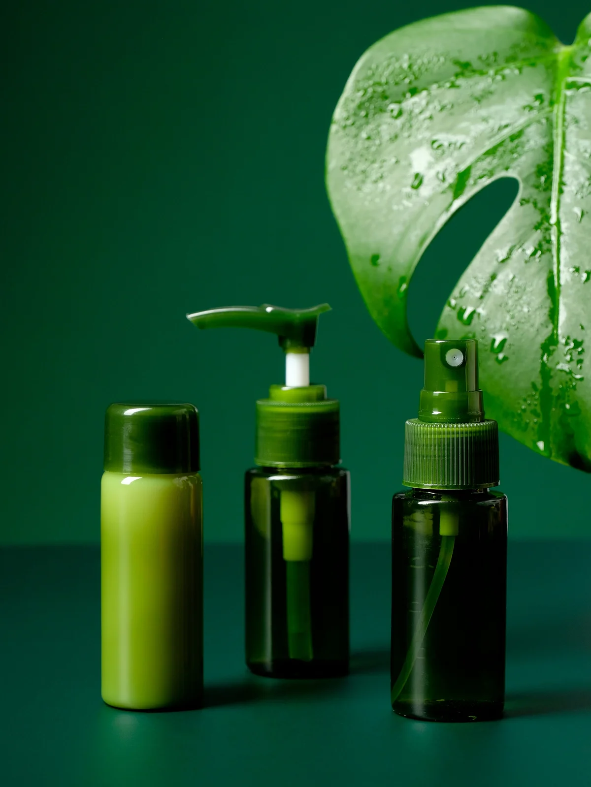 Produktaufnahme von drei beruhigenden Gels und Cremes in grünen Flaschen mit einem grossen tropischen grünen Blatt im Hintergrund