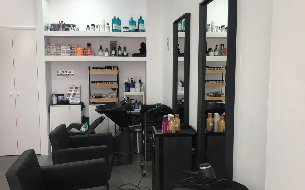 Ein Coiffeursalon mit schwarzen Waschstühlen und -becken, zwei hohen, schmalen Wandspiegeln und Regalen voller professioneller Farb- und Haarpflegeprodukte.